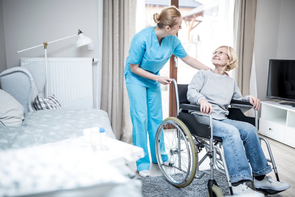 Senior woman in wheelchair with care worker in care home.